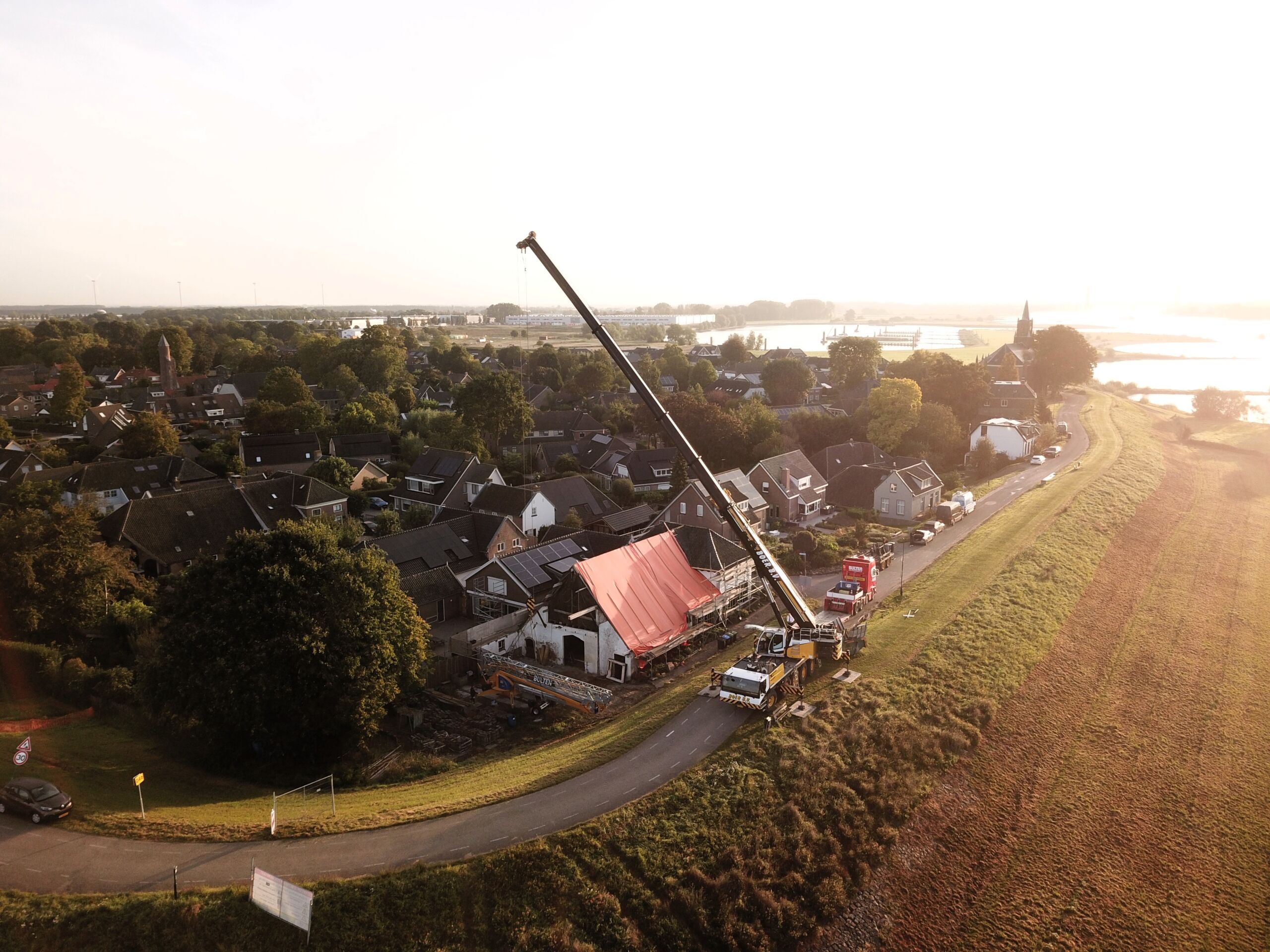 Gehuurde bouwkraan van Bulten Bouwkranen wordt met een telescoopkraan geplaatst op een bouwplek langs de dijk bij Haaften in Gelderland.
